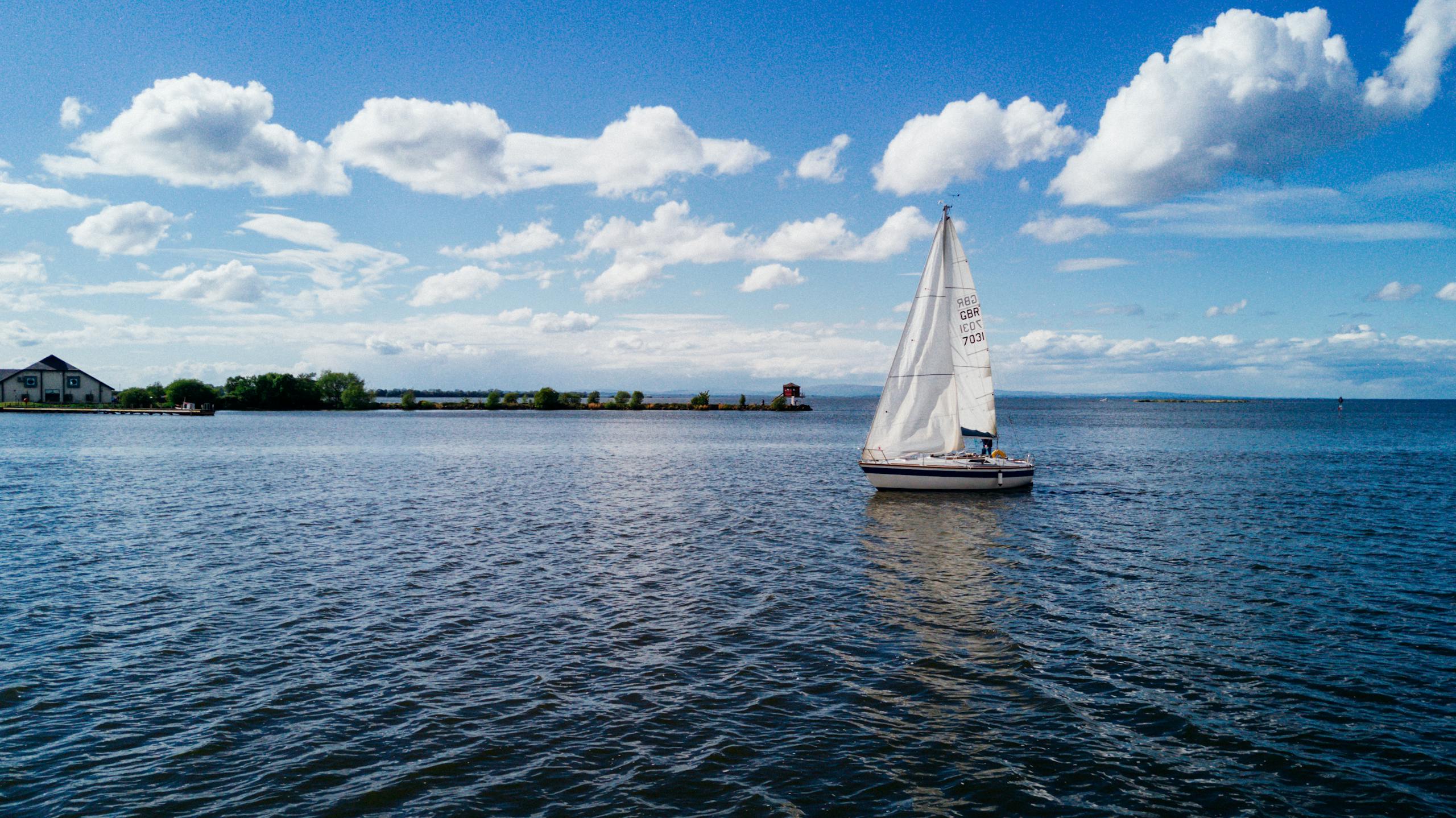 A serene scene with a white sailboat gliding across a calm sea under a bright blue sky.